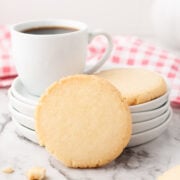 A close up of whipped shortbread cookies on a marble slab with plates and coffee off to the side