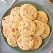 Peppermint sugar cookies piled on a green plate on a grey counter with candy canes on the side