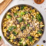 Ground Italian sausage, broccoli, orecchiette pasta, and black olives in a skillet.