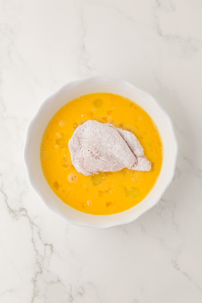  floured chicken cutlet being dipped in eggs