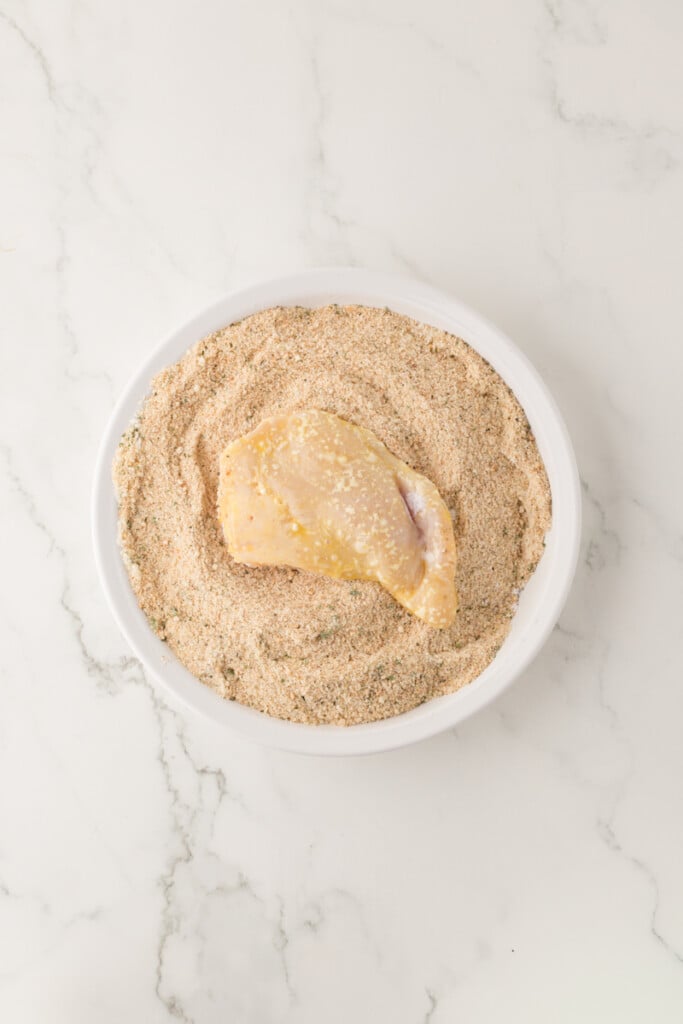 chicken cutlet being dipped into bread crumbs